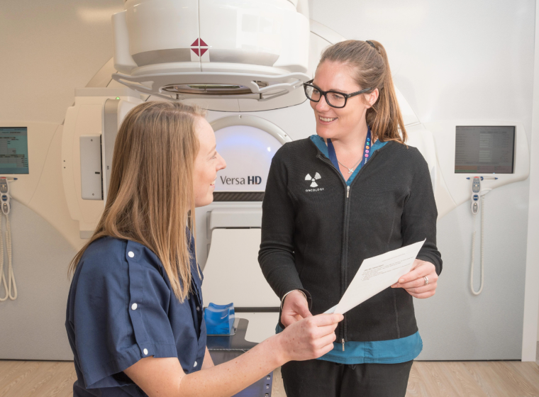 A radiation therapist and patient in front of a treatment machine and looking at paper.