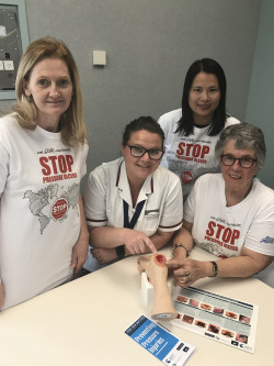 A group of nurses - all women - in white teeshirts with a mannequin foot with pressure injury sores on it
