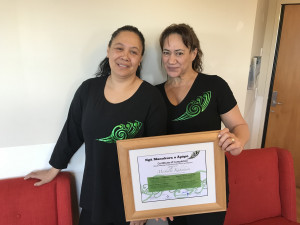 Two smiling women wearing black teeshirts hold a certificate of a course they have attended